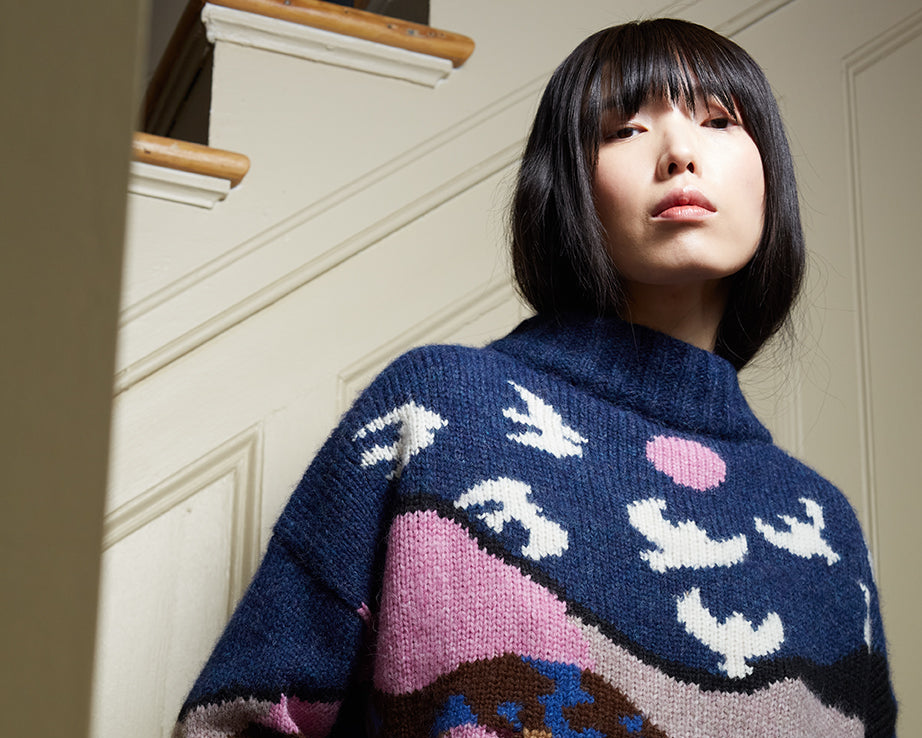 Person wearing a colorful patterned sweater standing indoors.
