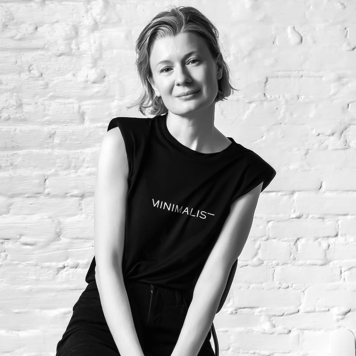 Person wearing a black sleeveless top with 'MINIMALIS' text against a white brick wall.