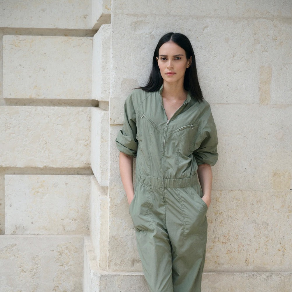 Woman wearing a green jumpsuit standing against a stone wall.